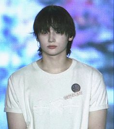 a young man with black hair and a white t - shirt is standing in front of a blue background