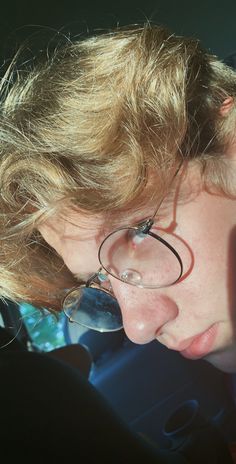 a young boy wearing glasses and looking at his cell phone in the back seat of a car