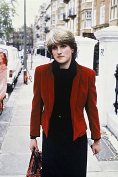 an older woman in a red jacket and black dress is walking down the street with her purse