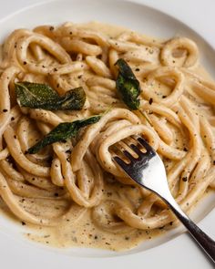 a white plate topped with pasta and spinach covered in gravy next to a fork