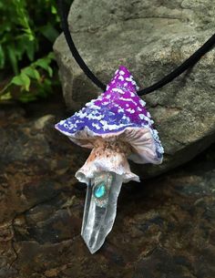 a necklace with a purple and blue hat on it sitting on top of a rock