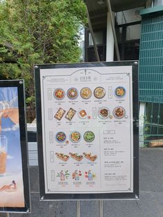 two signs with food on them sitting next to each other near a building and trees