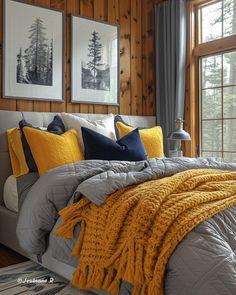 a bed with yellow and gray pillows in a bedroom next to two windows, framed pictures on the wall