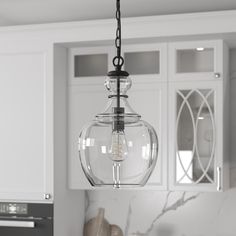 a clear glass light fixture hanging from a kitchen ceiling over a counter top with white cabinets