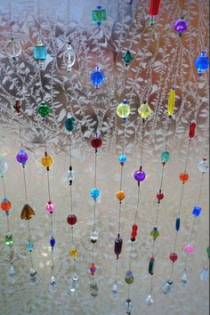 colorful glass beads hang from the ceiling in front of a frosted window pane