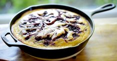 a skillet filled with food sitting on top of a wooden table next to a window