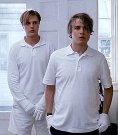 two men standing next to each other in front of a white door wearing gloves and polo shirts