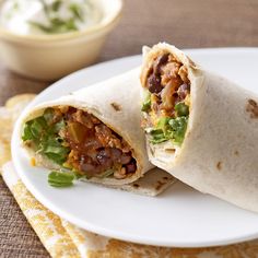 a burrito cut in half on a plate next to a small bowl of dip