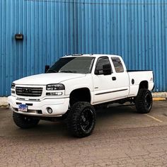 a white pick up truck parked in front of a blue metal building with black rims