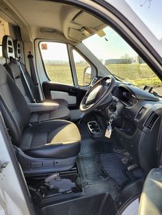 the interior of a white van with black leather seats and steering wheel, in front of a grassy field