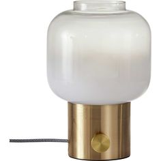 a glass and brass table lamp with a white light on it's base, next to a black cord