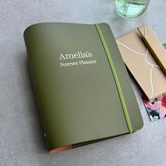 an open green book sitting on top of a table next to a pen and notebook