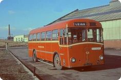 an orange bus parked in front of a building on the side of the road with no passengers