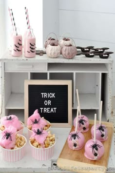 halloween treats are displayed on a table with pink cups and strawberries in front of them