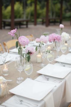 the table is set with white linens and pink flowers in vases, silverware, candles, napkins, and wine glasses