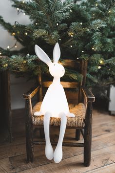 a white rabbit sitting on top of a wooden chair next to a christmas tree in a room