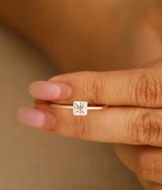 a woman's hand holding a ring with a small diamond on the middle of it