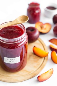 plum jam in a glass jar on a wooden plate with sliced peaches