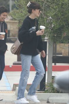 two people walking down the street with coffee in their hands and one holding a cell phone