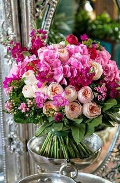 a vase filled with lots of pink flowers sitting on top of a metal tray next to a mirror