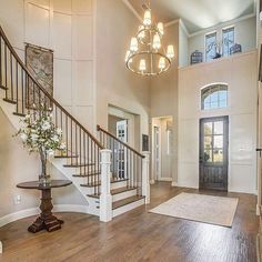 a large foyer with wooden floors and white walls, chandelier above the stairs