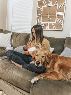 a woman sitting on a couch holding a baby and a golden retriever laying next to her