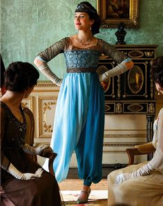 a woman in a blue dress standing next to two other women sitting down and talking