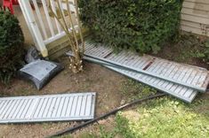 three metal steps are laying on the ground in front of a house with bushes and shrubbery