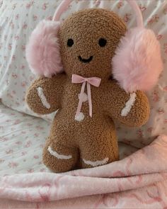 a brown teddy bear with pink ear muffs sitting on a bed