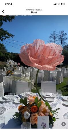 a large pink flower sitting on top of a table covered in white linens and place settings