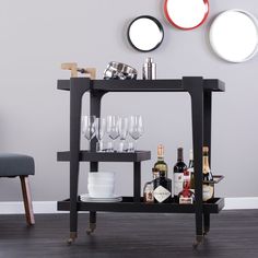 a bar cart with wine glasses and bottles on it in front of a gray wall