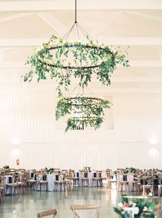 the tables are set up for an event with greenery hanging from the chandelier