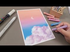 someone is drawing clouds with crayons on the table next to some markers and pencils