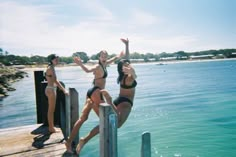 three women in bathing suits jumping off a dock into the water from a pier on a sunny day