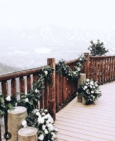 a wooden deck with white flowers and greenery on the railing, surrounded by snow covered mountains