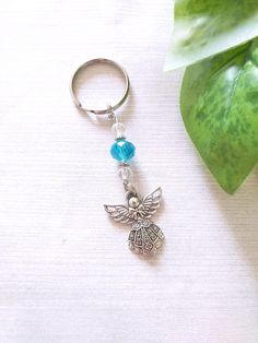 a silver keychain with a blue beaded angel charm on it next to a green plant