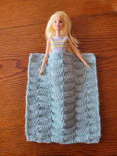 a doll laying on top of a blue knitted blanket next to a wooden table