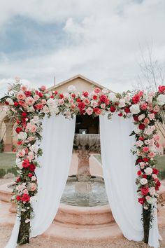 an outdoor wedding ceremony with flowers on the arch and white drapes over the fountain