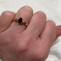 a person's hand holding a gold ring with a garnet stone on it