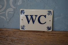 a white and blue ceramic sign with the letter wc on it's side