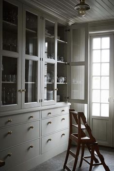 a white china cabinet with glass doors and drawers in a room that has light coming through the windows