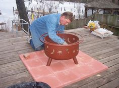 a man in blue shirt and jeans bending over a large pot on top of a wooden deck