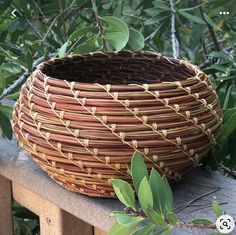 a woven basket sitting on top of a wooden table next to green leaves and branches