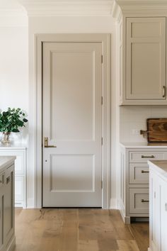 an open door in a white kitchen with wood flooring and cabinets on either side