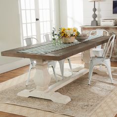 a dining room table with white chairs and flowers on the top, in front of a window