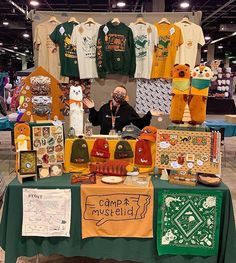 a man standing in front of a green table covered with shirts and other items on display