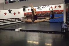 two young women are doing acrobatic tricks on a stage in a gym