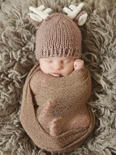 a baby is wearing a knitted deer hat and sleeping on a pile of carpet