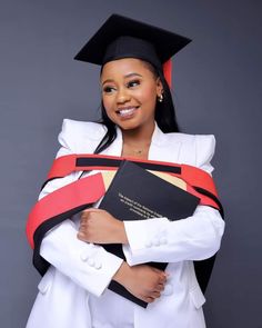 a woman wearing a graduation gown and holding a book in her arms, smiling at the camera