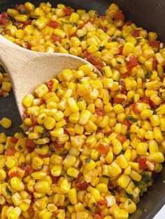 a wooden spoon is full of corn and tomato mixture in a skillet on the stove